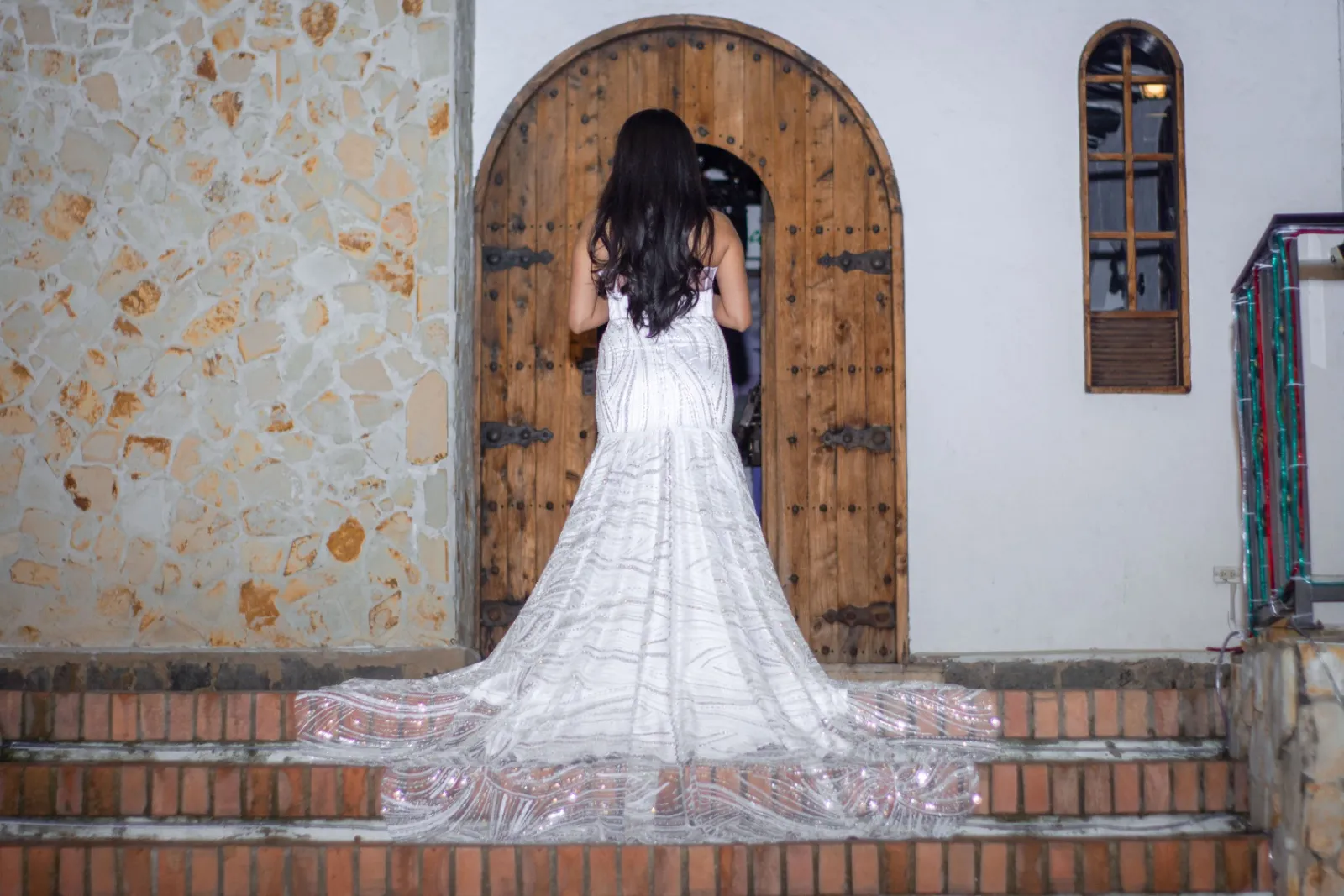 Mujer con vestido blanco bordado de espaldas frente a una puerta de madera