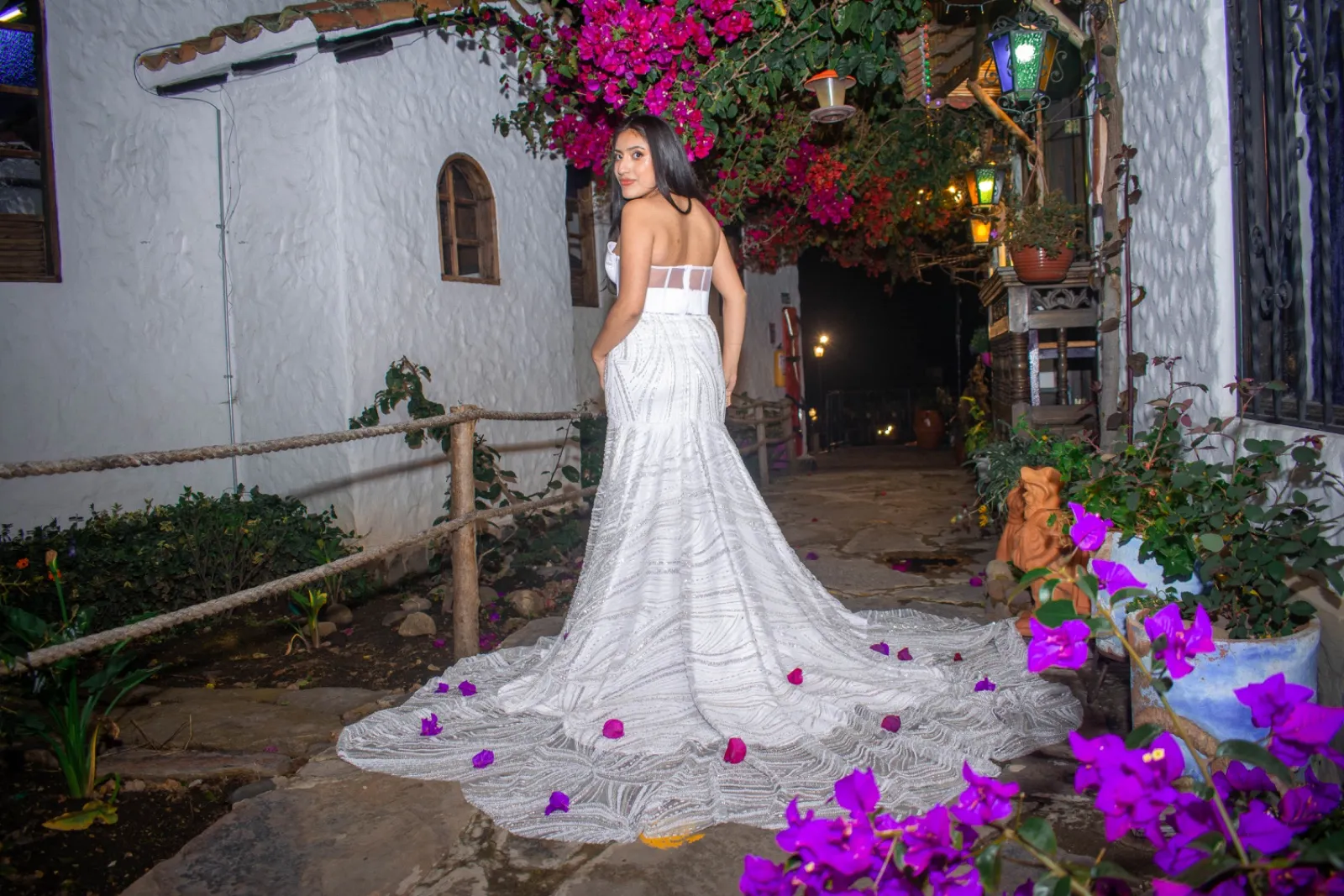 Mujer con vestido blanco bordado y cola entre buganvilias