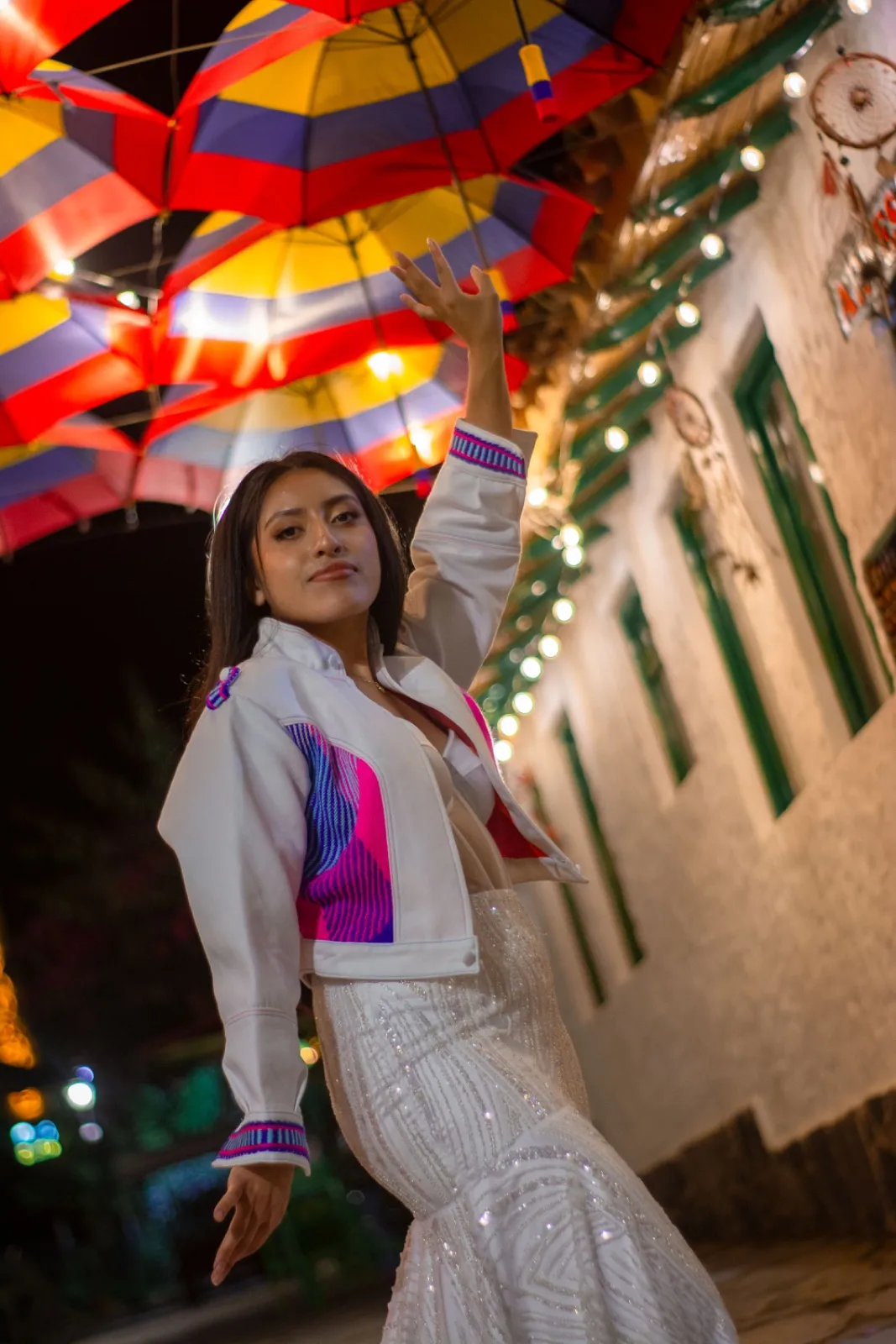 Mujer con chaqueta blanca de detalles rosa y azul sobre vestido blanco bordado
