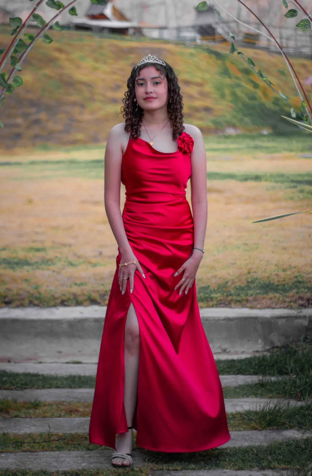 Quinceañera con vestido rojo de satín frente a un arco decorado