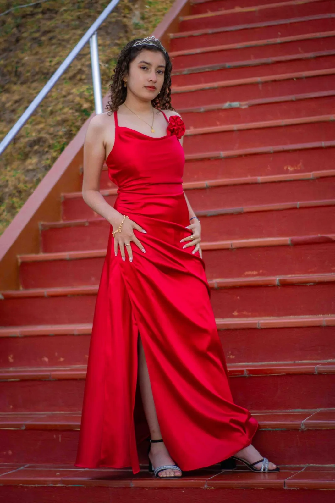 Quinceañera con vestido rojo de satín sobre escaleras rojas, con las manos en la cintura