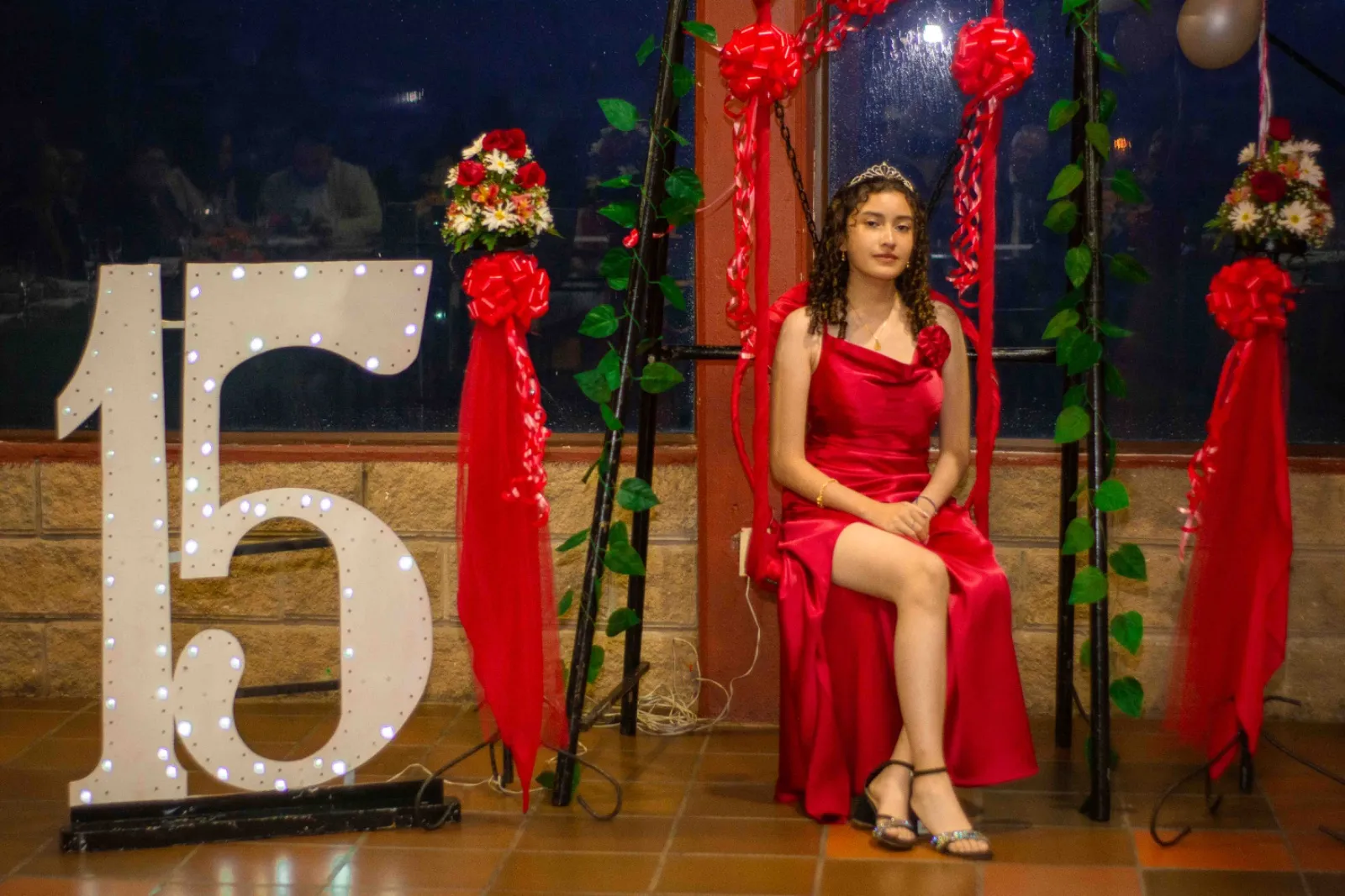 Quinceañera con vestido rojo de satín sentada en un columpio decorado