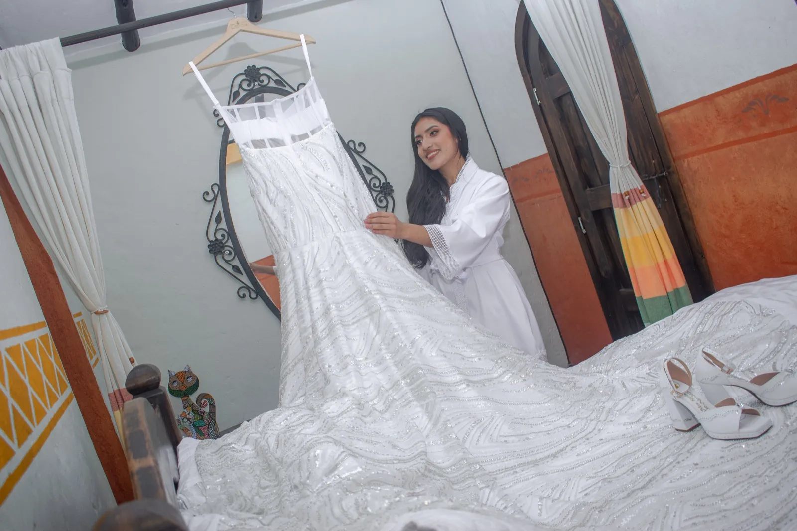 Novia en bata junto al vestido blanco colgado, con la cola extendida en el suelo